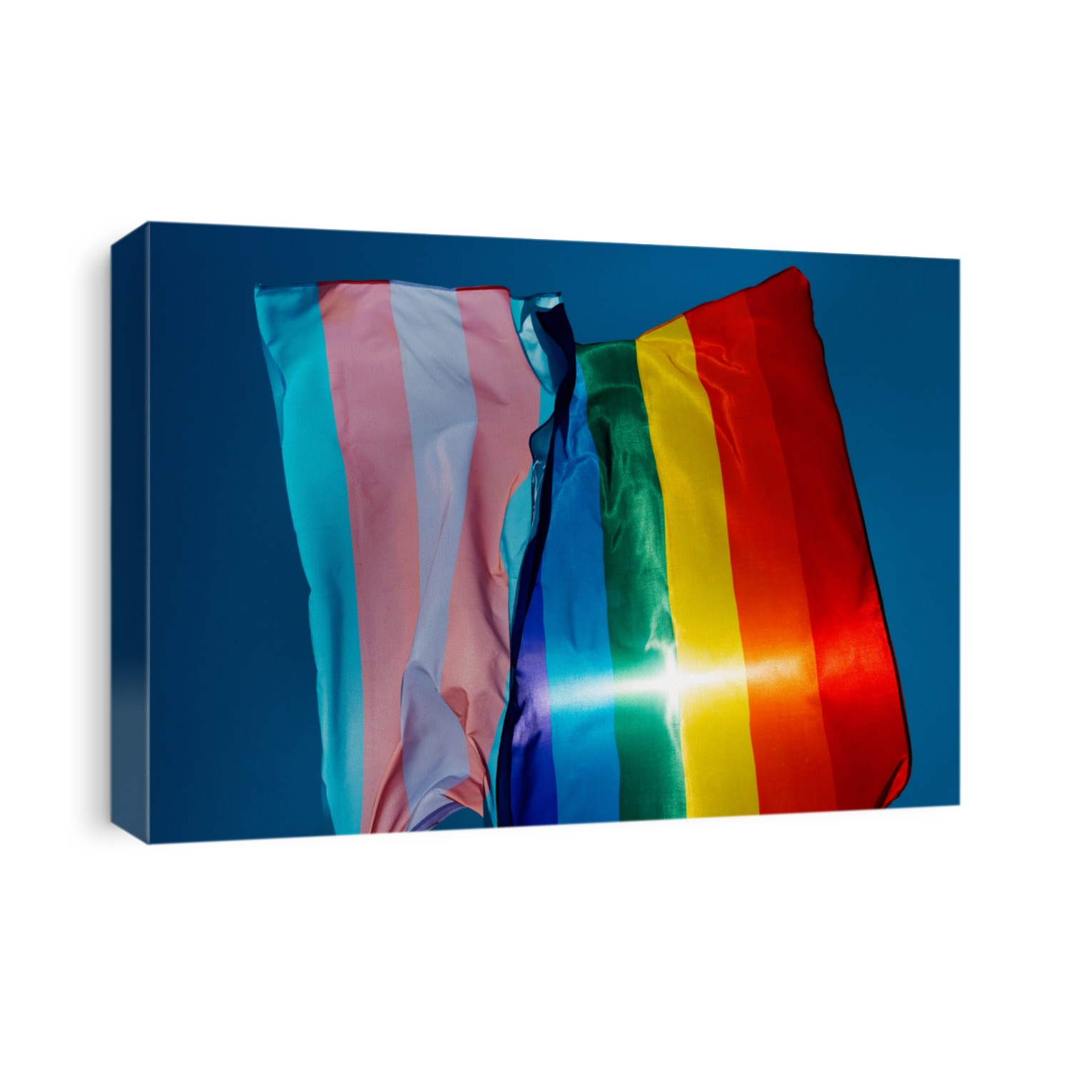 closeup of a gay pride flag and a transgender pride flag waving on the blue sky, moved by the wind, with the sun in the background
